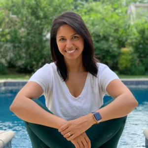 Priyanka Venugopal near a pool, dressed casually in a white t-shirt, green yoga pants, and complemented by a sleek smart watch