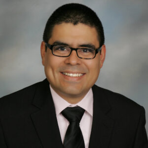 Miguel Villagra MD emanating professionalism in a black coat and necktie, his smart look accentuated by eyeglasses