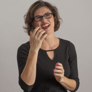Jackie Wiebe, a vibrant life coach with black long sleeves, eyeglasses, and red lipstick, radiates positivity in a fun-loving studio shot.